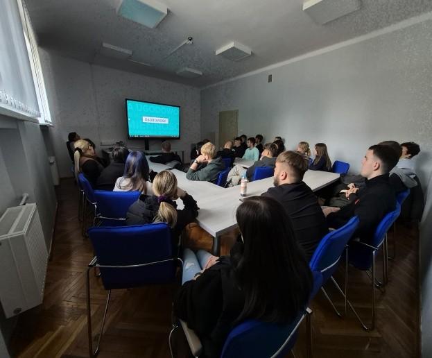 Fotografia wykonana podczas spotkania doradców zawodowych z uczniami Zespołu Szkół im. X. Dunikowskiego w  Zawierciu. Przedstawia salę wykładową a w niej grupę uczniów siedzących przy stołach i słuchających prezentacji.