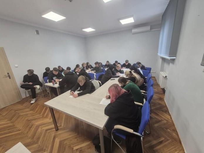 Fotografia wykonana podczas spotkania doradców zawodowych z uczniami Zespołu Szkół im. X. Dunikowskiego w  Zawierciu. Przedstawia salę wykładową a w niej grupę uczniów siedzących przy stołach i słuchających prezentacji.