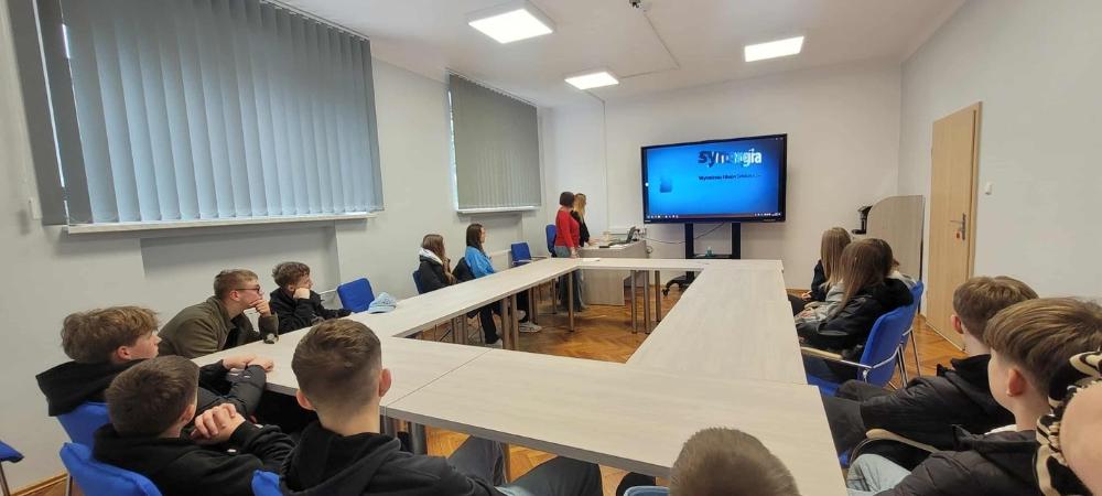 Fotografia wykonana podczas spotkania z uczniami SP 9, przedstawia salę wykładową a w niej uczniów siedzących przy stołach, uczestniczących w prelekcji prowadzonej przez pracownice PUP.