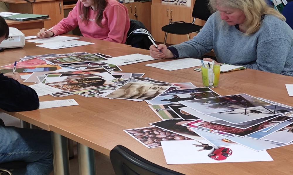 Fotografia wykonana podczas warsztatów, przedstawia uczestniczki spotkania siedzące przy stołach na których rozłożone są materiały dydaktyczne.