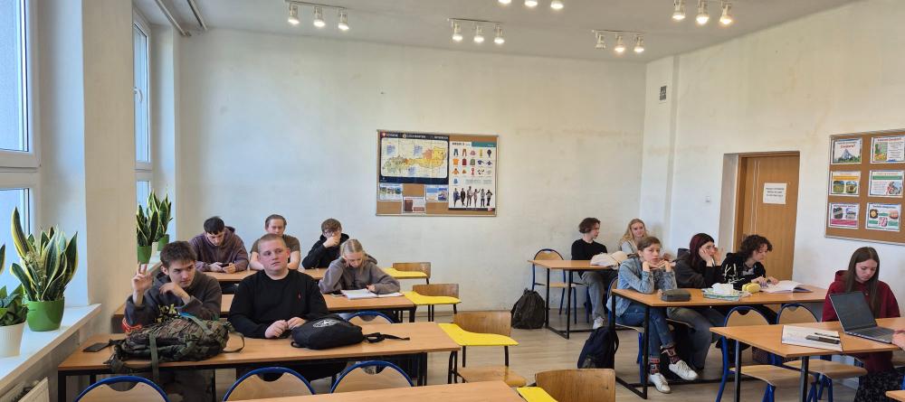 Fotografia przedstawia klasę lekcyjną a w niej uczniów siedzących przy ławkach.