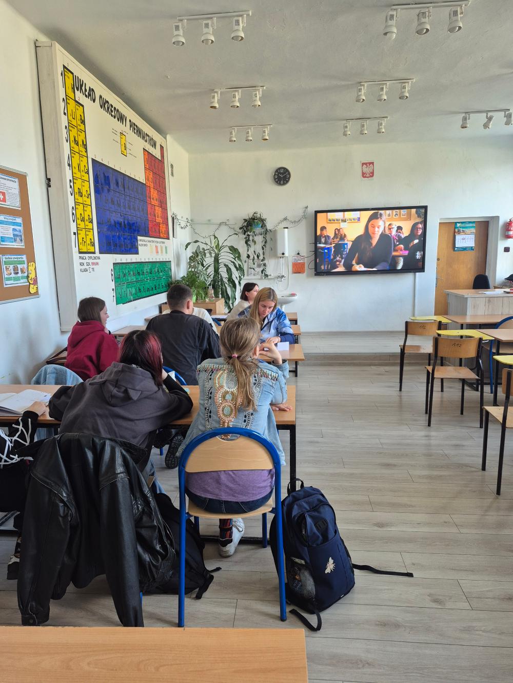 Fotografia przedstawia klasę lekcyjną a w niej uczniów siedzących przy ławkach.
